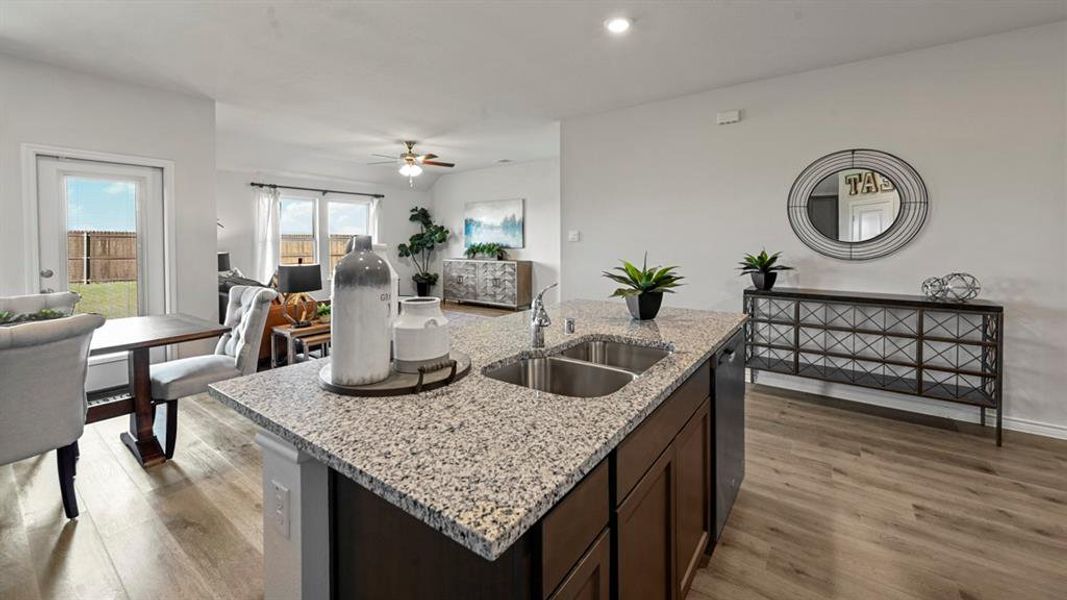 Kitchen with light stone countertops, open floor plan, dark brown cabinets, light wood finished floors, and recessed lighting