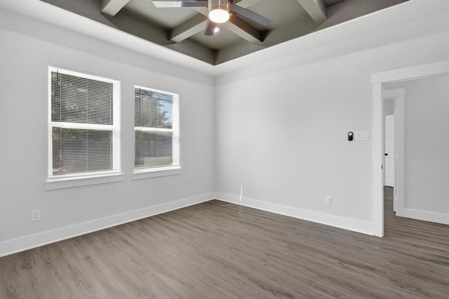 Spacious room featuring a decorative tray ceiling with a ceiling fan, two windows, wood-finish flooring, and crisp white baseboards