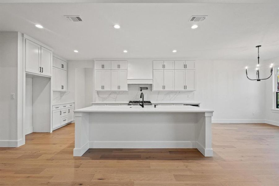 Kitchen featuring white cabinets, a breakfast bar area, recessed lighting, an island with sink, and light wood-style floors