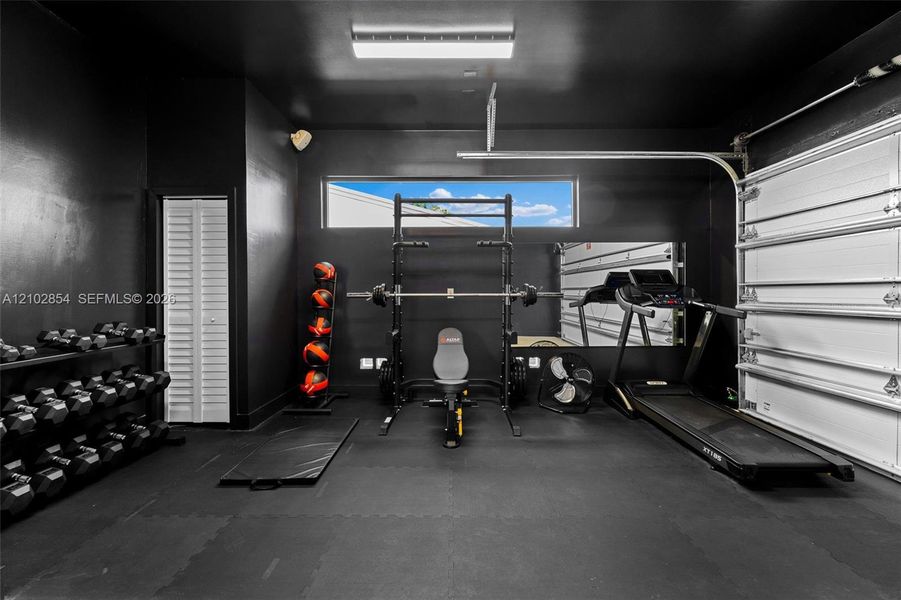 Multi-purpose space featuring matte black walls, a horizontal clerestory window, recessed overhead lighting, and a white paneled garage door