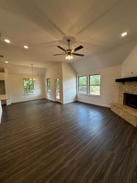 Unfurnished living room with a wealth of natural light, ceiling fan, dark wood-type flooring, and vaulted ceiling