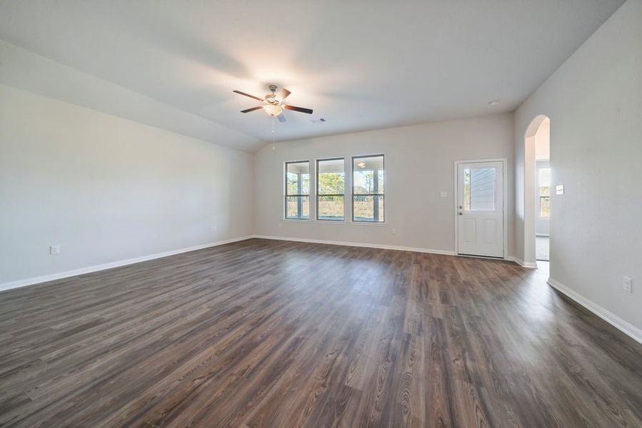 Empty living room with laminate flooring, ceiling fan, and three windows