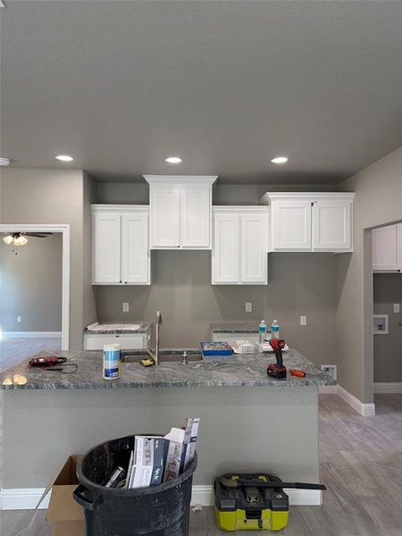 Kitchen with light stone countertops, light wood finished floors, a kitchen island with sink, white cabinetry, and recessed lighting Kitchen with light stone countertops, light wood finished floors, a kitchen island with sink, white cabinetry, and recessed lighting