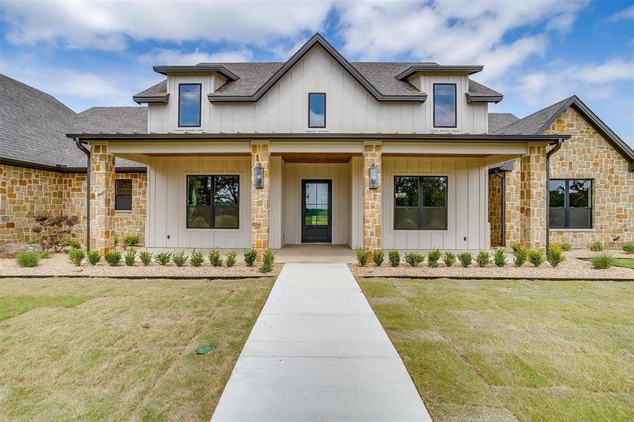 Modern farmhouse style home with roof with shingles, stone siding, covered porch, and board and batten siding Modern farmhouse style home with roof with shingles, stone siding, covered porch, and board and batten siding
