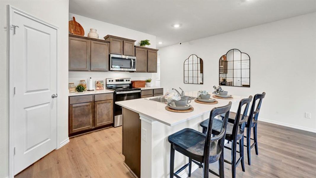 Kitchen featuring stainless steel appliances, an island with sink, a kitchen breakfast bar, dark wood finish cabinets, and light wood finished floors