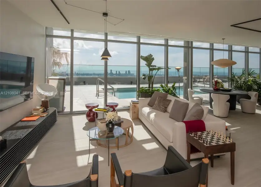 Expansive floor-to-ceiling windows, outdoor pool deck, integrated ceiling lighting, light-toned flooring, and a contemporary pendant fixture