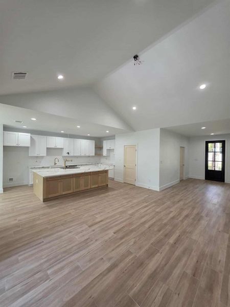 Kitchen with open floor plan, white cabinetry, vaulted ceiling, light wood-type flooring, and recessed lighting