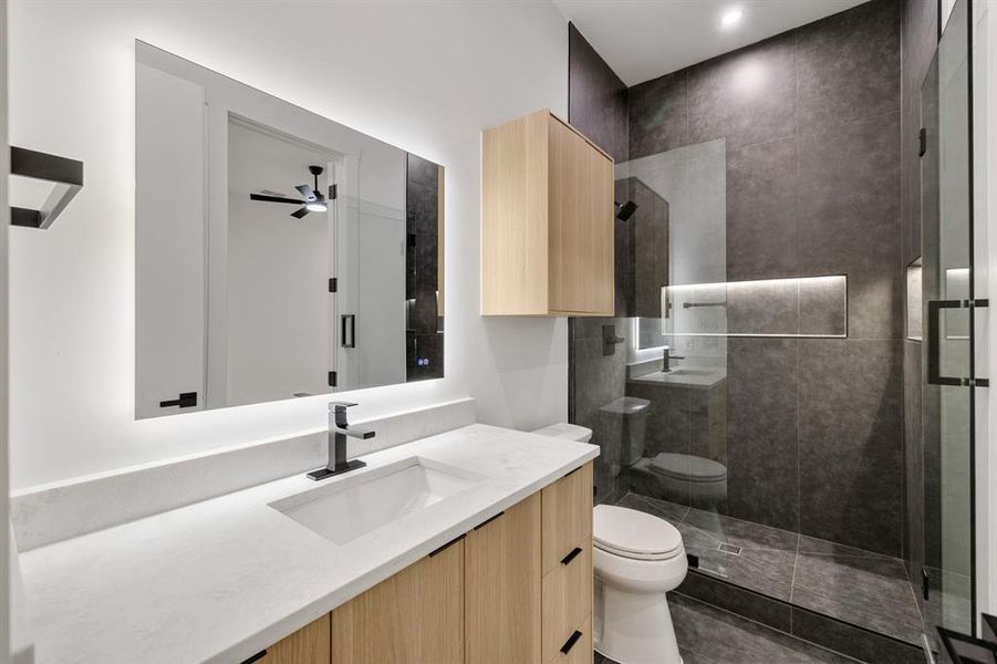 Bathroom featuring a light wood-finish vanity with a white countertop and integrated sink, back-lit mirror, and matte black fixtures