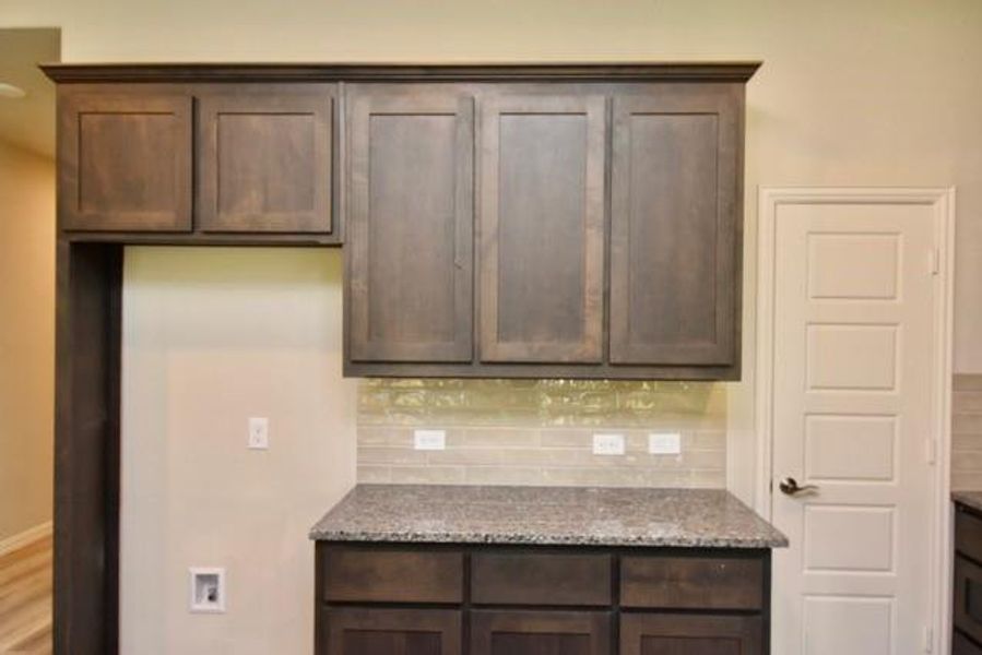 Kitchen with tasteful backsplash, dark brown cabinets, and light stone counters Kitchen with tasteful backsplash, dark brown cabinets, and light stone counters