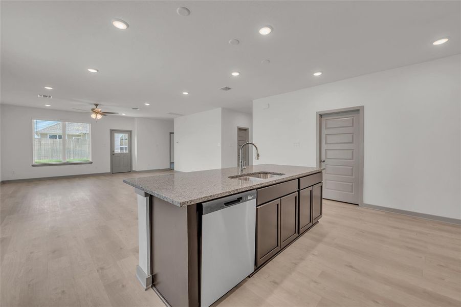 Kitchen featuring dishwasher, a kitchen island with sink, recessed lighting, light wood finished floors, and light stone countertops