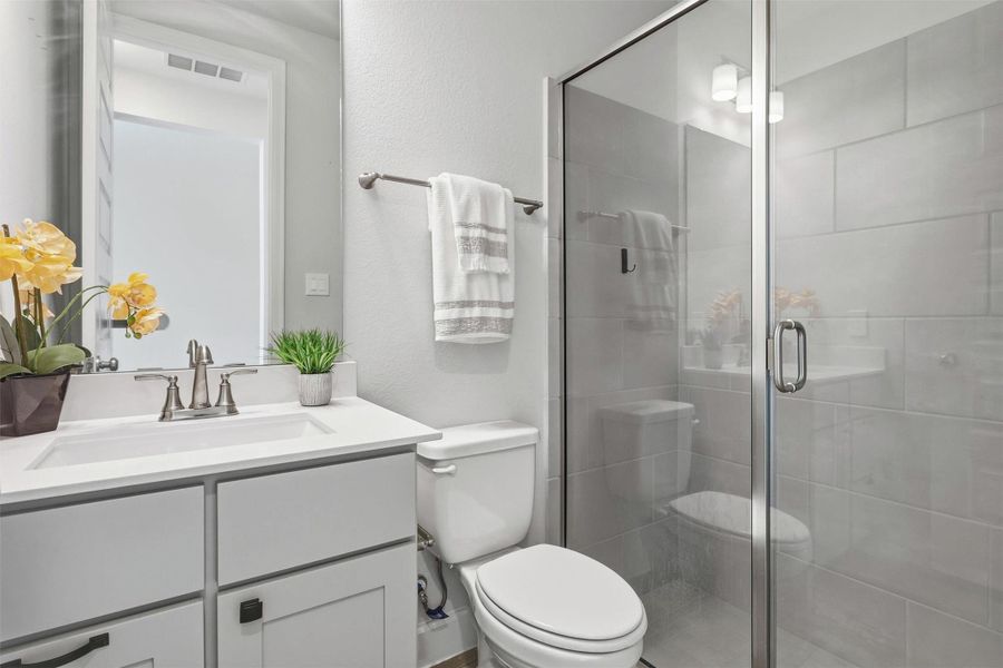 A beautifully appointed secondary bathroom features a sleek quartz vanity, shaker-style cabinetry, designer lighting, and a spacious glass-enclosed walk-in shower with oversized tile, offering guests and family a stylish, comfortable retreat.