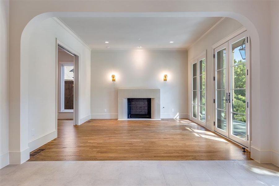 Unfurnished living room with arched walkways, a fireplace with flush hearth, crown molding, light wood-type flooring, and recessed lighting Unfurnished living room with arched walkways, a fireplace with flush hearth, crown molding, light wood-type flooring, and recessed lighting