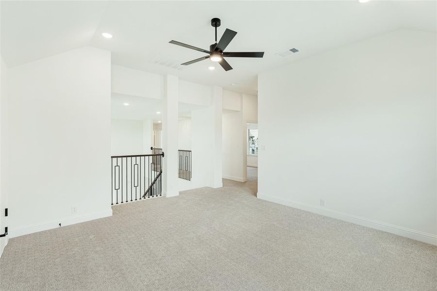 Open upstairs loft with carpet flooring, ceiling fan, and iron stair railing overlooking lower level