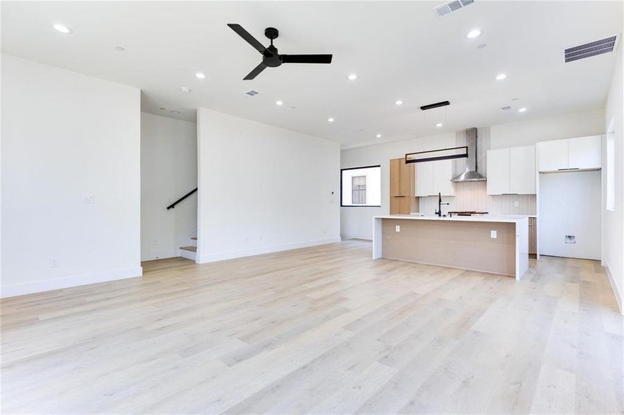 Kitchen with decorative light fixtures, white cabinetry, a kitchen island with sink, ceiling fan, and wall chimney range hood