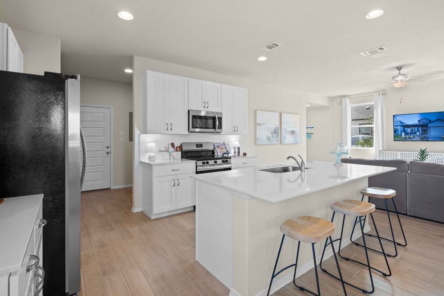 An interior image of a kitchen with white marble counter top and island, vinyl flooring, white cabinets, and steel refrigerator and dishwashers and a black and steel stove. An interior image of a kitchen with white marble counter top and island, vinyl flooring, white cabinets, and steel refrigerator and dishwashers and a black and steel stove.