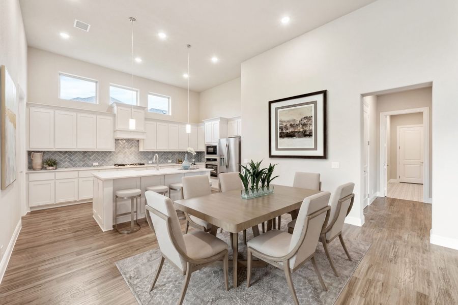 Open-concept dining area and kitchen with white cabinets, herringbone backsplash, and hardwood floors