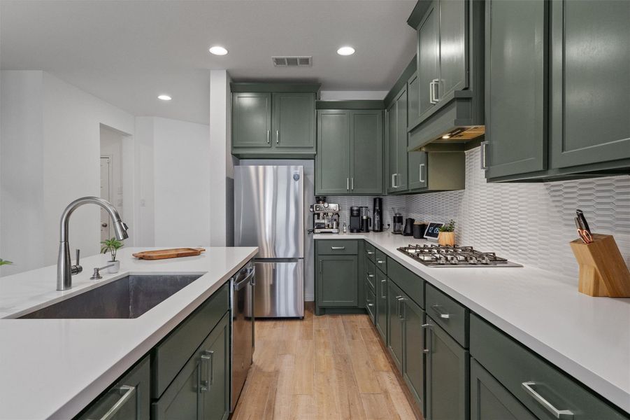 Kitchen featuring green cabinetry, light wood-type flooring, stainless steel appliances, recessed lighting, and light stone counters