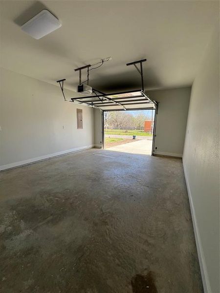 Garage featuring electric panel, a garage door opener, and baseboards