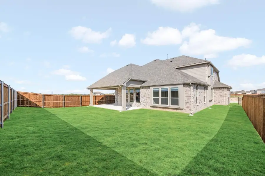 Backyard of two-story brick home with covered patio, green lawn, and wood privacy fence