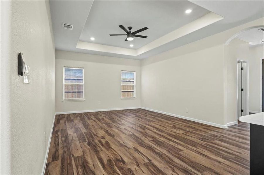 Empty room featuring dark wood-style flooring, a raised ceiling, arched walkways, a ceiling fan, and recessed lighting Empty room featuring dark wood-style flooring, a raised ceiling, arched walkways, a ceiling fan, and recessed lighting