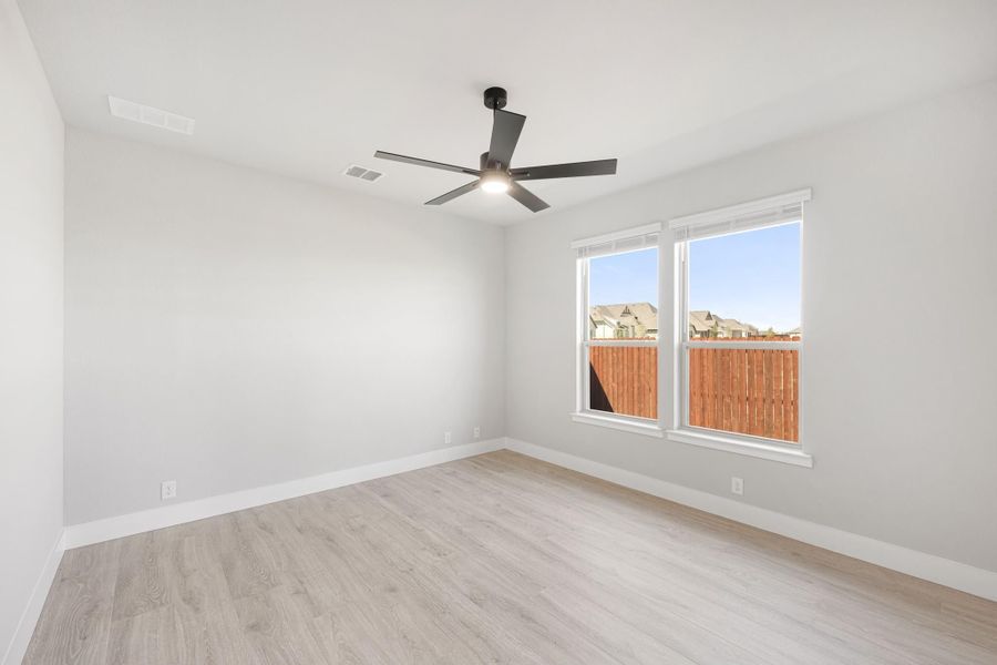 Empty bedroom with light wood floors, ceiling fan, and double windows overlooking a wood fence Empty bedroom with light wood floors, ceiling fan, and double windows overlooking a wood fence