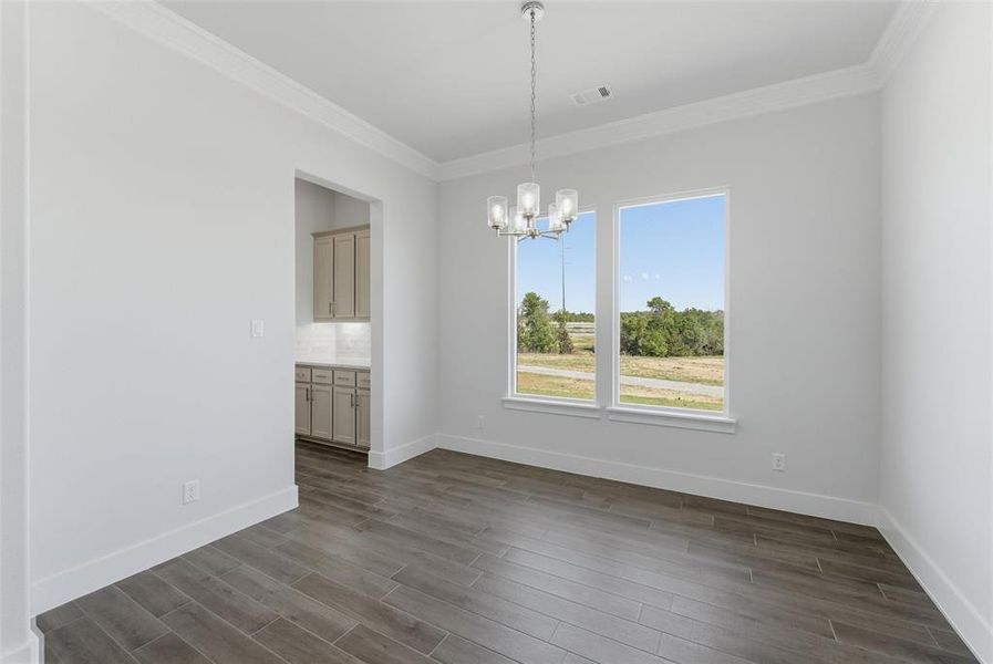 Unfurnished dining area with a chandelier, dark wood-type flooring, and ornamental molding