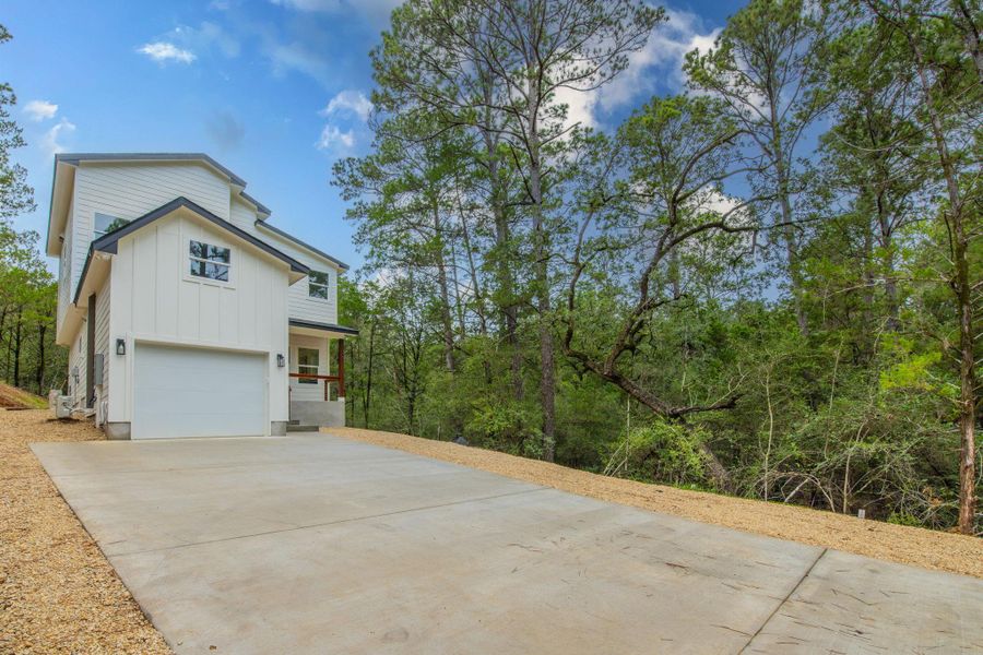 A newly constructed residence is nestled among a verdant forest, featuring a concrete driveway leading to a garage. A newly constructed residence is nestled among a verdant forest, featuring a concrete driveway leading to a garage.