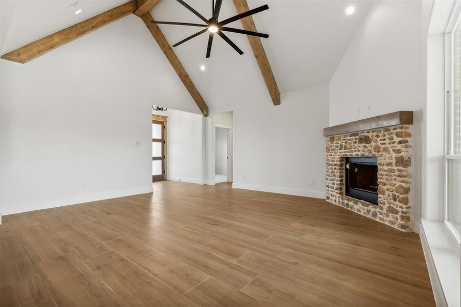 Unfurnished living room with light wood-type flooring, ceiling fan, beam ceiling, and a brick fireplace