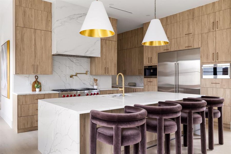 Kitchen featuring a kitchen island with sink, a sink, stainless steel built in refrigerator, modern cabinets, and decorative light fixtures