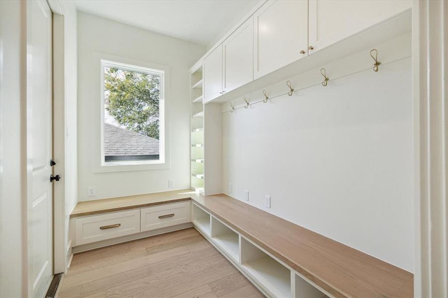 Functional and stylish, the mudroom offers a well-designed space to keep everyday essentials organized. Built-in cabinets and open shelving provide ample storage, while a bench with lower cubbies and pull-out drawers ensures convenience and efficiency. A row of brass hooks adds a touch of elegance, perfect for hanging coats, bags, or accessories. The thoughtful layout makes this mudroom an essential hub for managing busy routines.