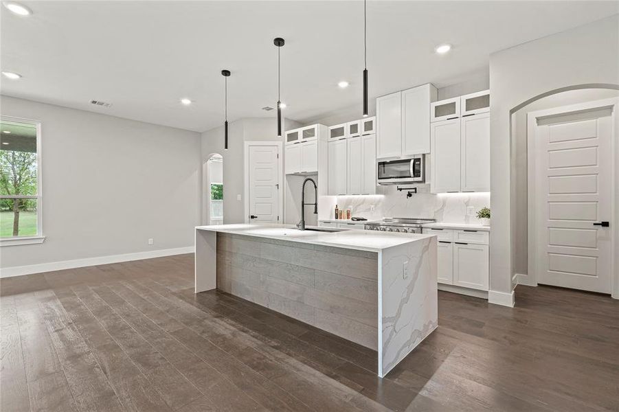 Kitchen featuring appliances with stainless steel finishes, arched walkways, dark wood finished floors, an island with sink, and recessed lighting