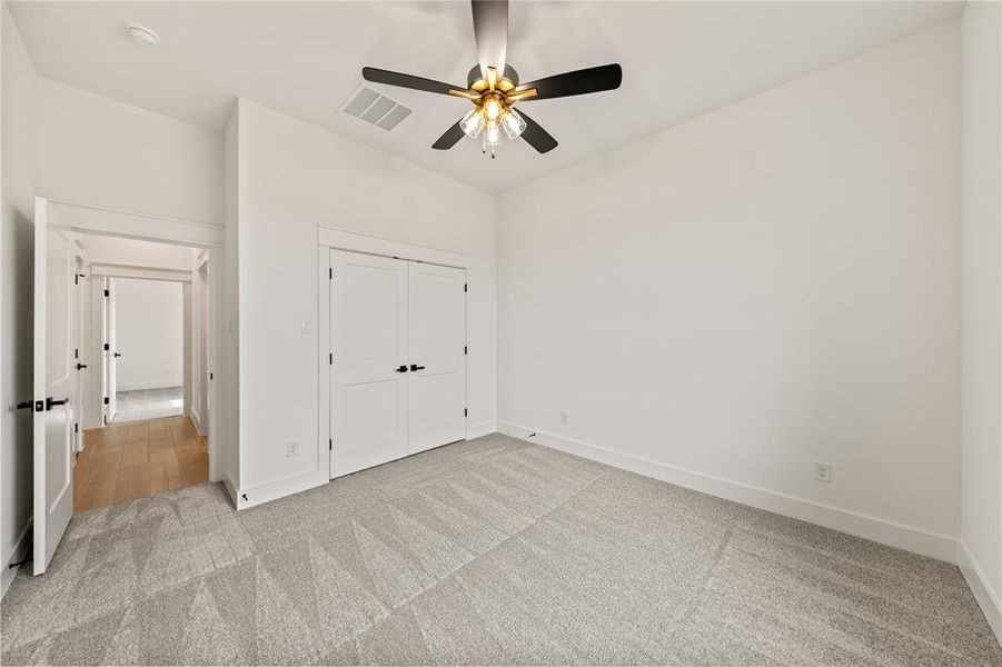 Neutral-toned room featuring a ceiling fan with black blades and brass accents, light gray patterned carpeting, white walls, and white trim