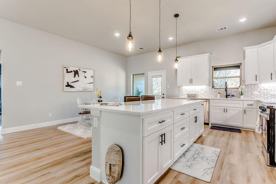 Kitchen with decorative backsplash, light wood-type flooring, white cabinets, a center island, and hanging light fixtures