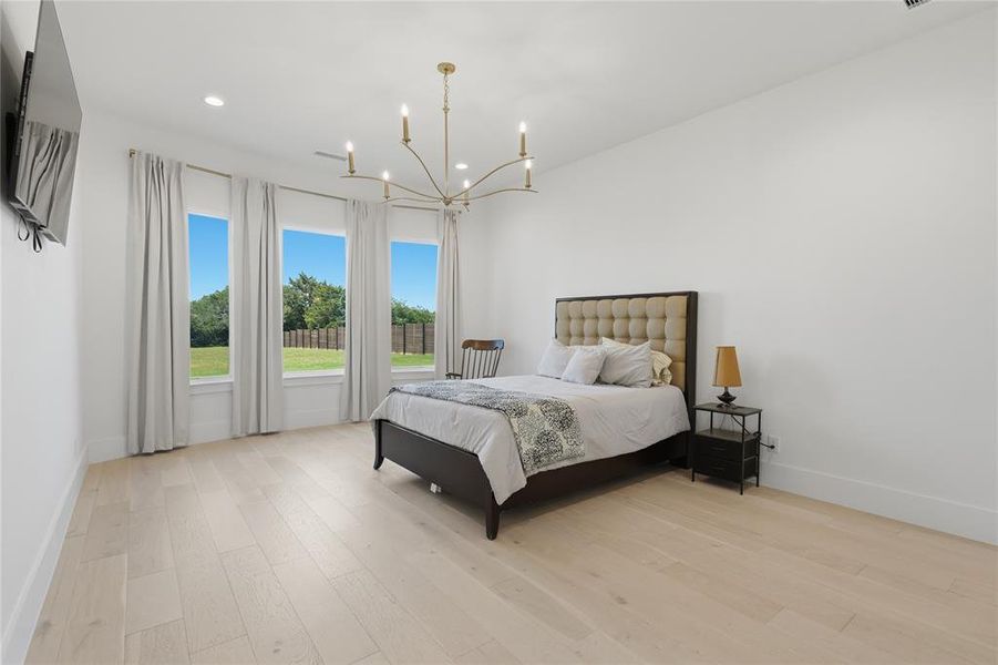 Expansive room featuring light wood-finish flooring, recessed lighting, and a modern gold-toned chandelier