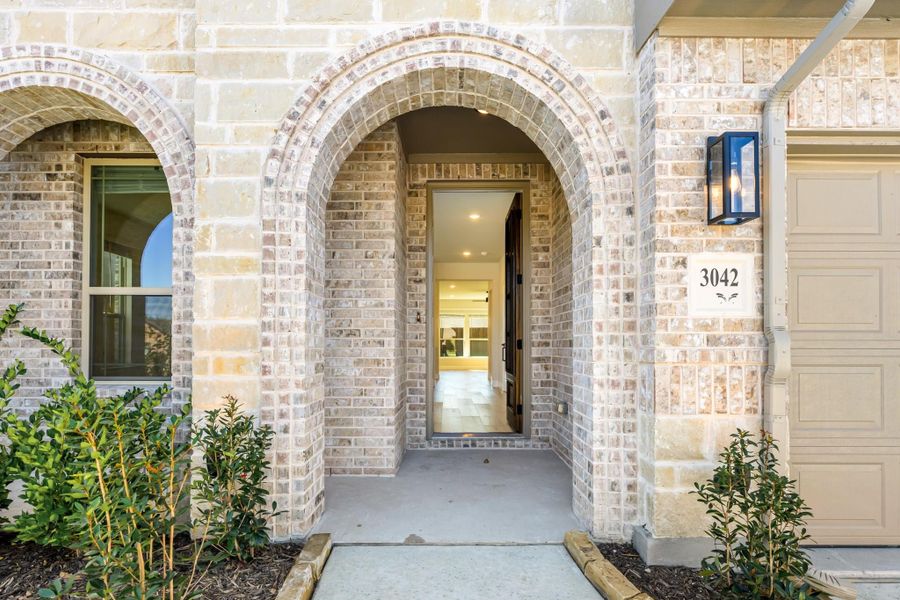 Brick home entrance with arched doorway, wall sconce, and house number 3042 beside a garage door
