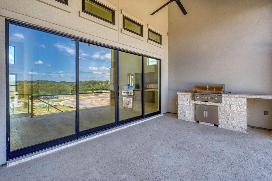 A spacious covered back porch features a built-in stone grill station and towering sliding doors.