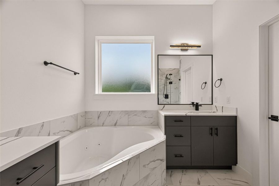 This bathroom features a modern design with a luxurious corner whirlpool tub, marble-style tile, a sleek black vanity with a large mirror, and a frosted window for privacy. This bathroom features a modern design with a luxurious corner whirlpool tub, marble-style tile, a sleek black vanity with a large mirror, and a frosted window for privacy.