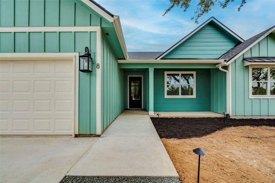 Doorway to property featuring board and batten siding, an attached garage, and a shingled roof