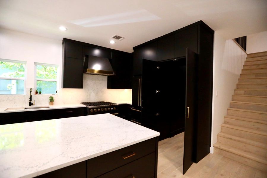 Kitchen with dark cabinets, light stone counters, tasteful backsplash, light wood-style floors, and black gas stovetop