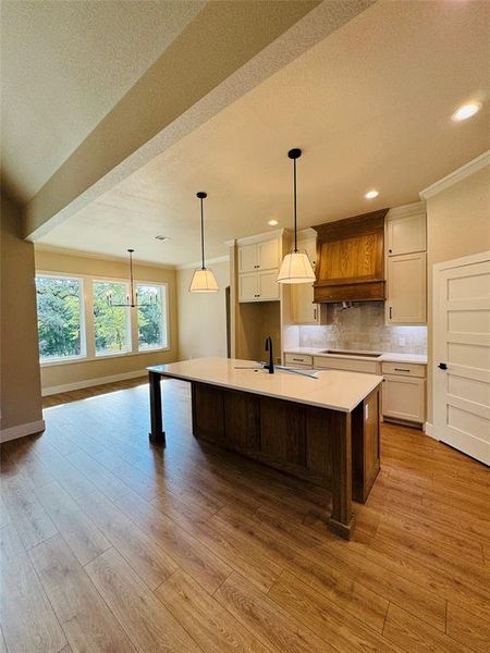 Kitchen with pendant lighting, decorative backsplash, a kitchen island with sink, light wood finished floors, and a textured ceiling Kitchen with pendant lighting, decorative backsplash, a kitchen island with sink, light wood finished floors, and a textured ceiling