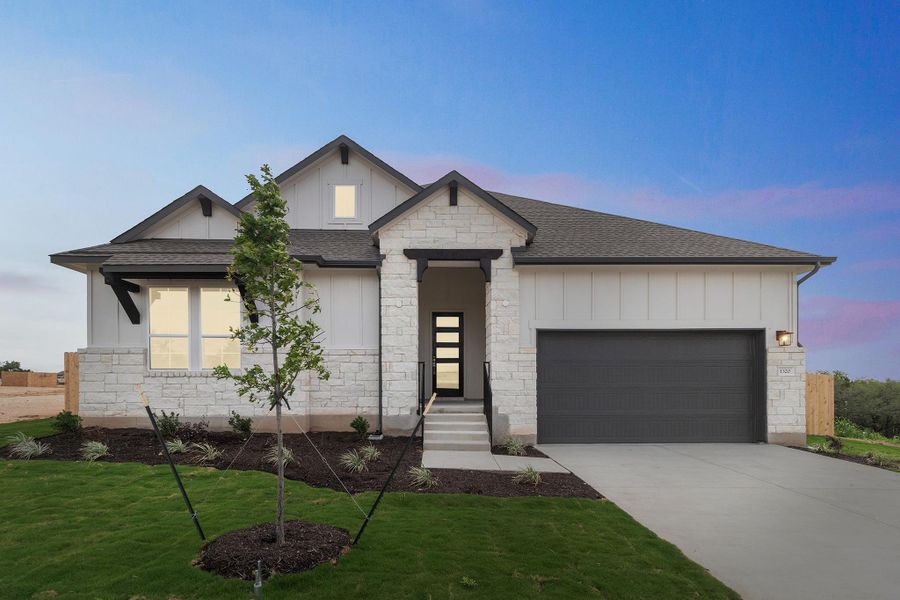 View of front of property with board and batten siding, an attached garage, driveway, and stone siding
