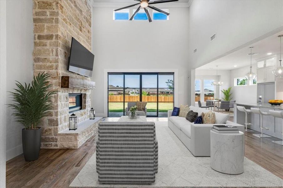 Living room featuring ornamental molding, a stone fireplace, light hardwood / wood-style flooring, a high ceiling, and ceiling fan with notable chandelier