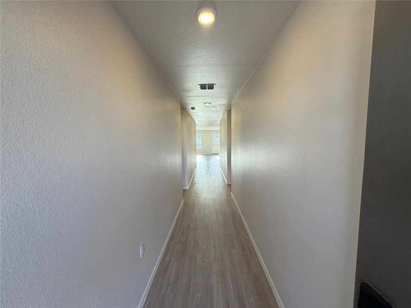 Smooth wood-look flooring guides the eye down a long, neutral-toned hallway.