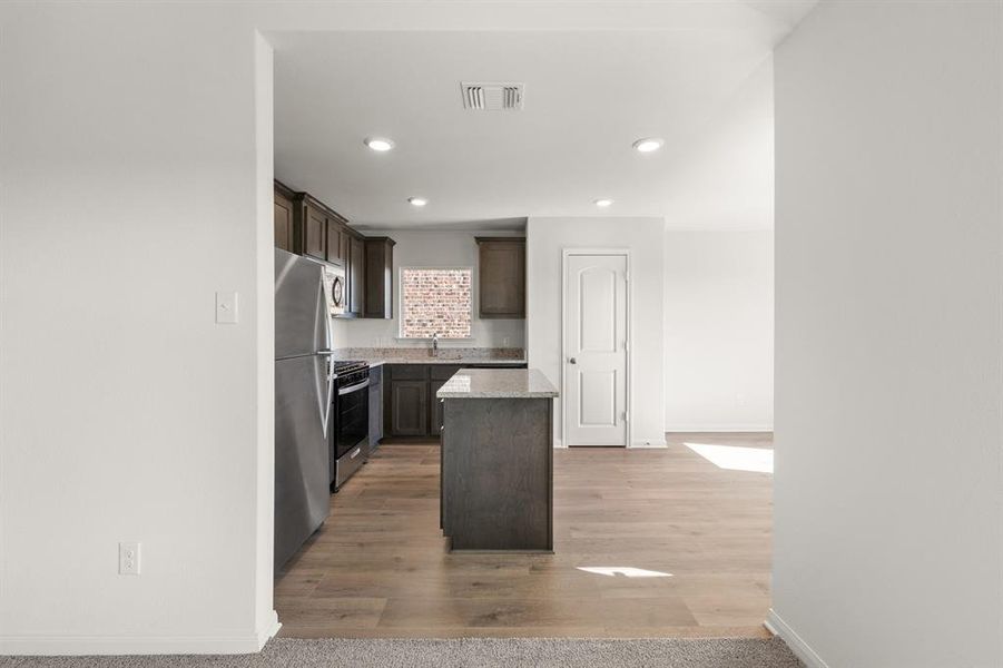 Kitchen featuring a kitchen island, dark brown cabinetry, recessed lighting, stainless steel appliances, and light wood-style flooring