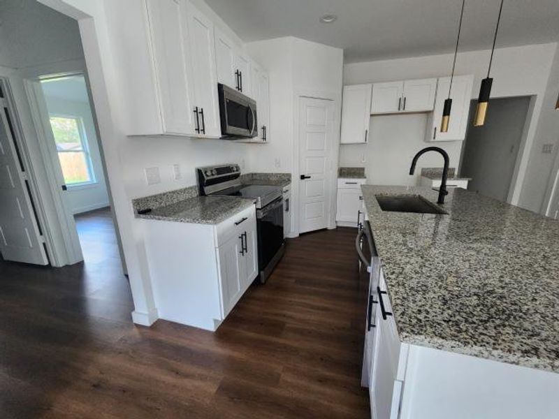 Kitchen featuring stainless steel appliances, light stone countertops, hanging light fixtures, white cabinetry, and dark wood-style floors Kitchen featuring stainless steel appliances, light stone countertops, hanging light fixtures, white cabinetry, and dark wood-style floors