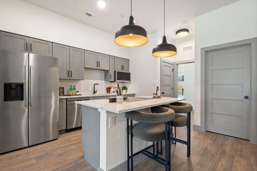 Kitchen featuring stainless steel appliances, hanging light fixtures, light wood-style floors, and gray cabinets