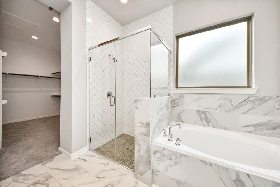 Primary bathroom featuring a glass-enclosed walk-in shower, soaking tub with elegant marble-look surround, frosted window for natural light, and direct access to a spacious walk-in closet.