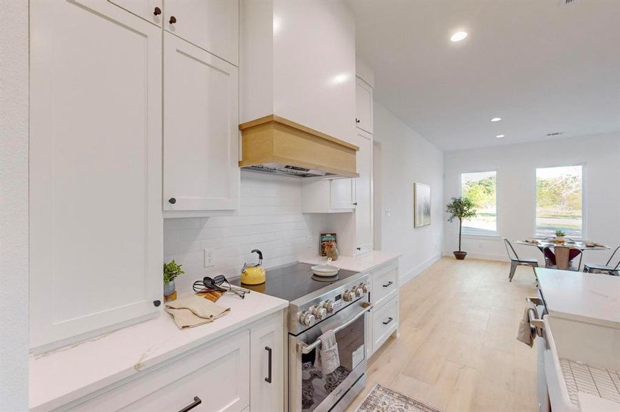 Kitchen featuring tasteful backsplash, white cabinetry, custom exhaust hood, high end range, and light hardwood / wood-style flooring