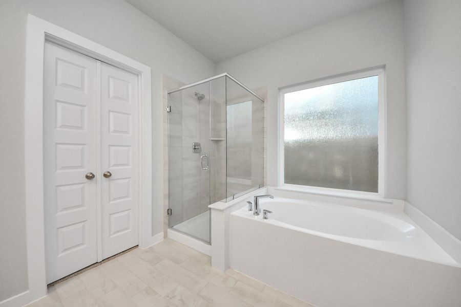 Indulge in a spa-like retreat within the confines of this primary bathroom. Delight in a spacious walk-in shower enveloped in stylish tile surround, unwind in a separate garden tub adorned with custom detailing. Sample photo of completed home with similar floor plan. Actual colors and selections may vary.