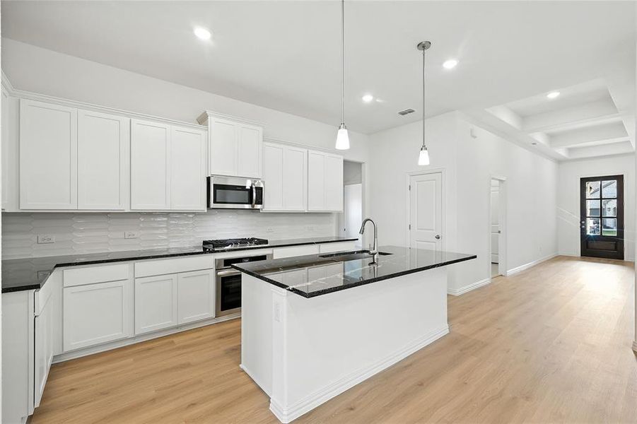 Kitchen with light wood-style floors, a center island with sink, white cabinetry, dark stone counters, and stainless steel appliances